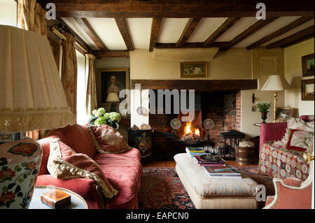 Inglenook Kamin im gemütlichen Wohnzimmer mit original Balkendecke und rotes sofa Stockfoto