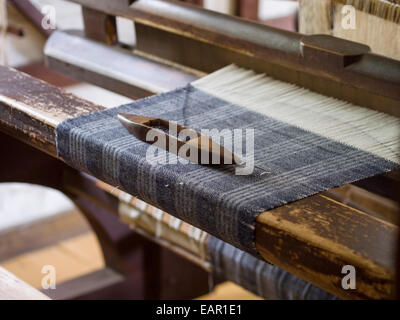 Federball auf einen Tartan zu weben. Ein Federball mit blauer Wolle ruht auf einem Tartan Stück Stoff wird auf einem Vintage home Webstuhl gewebt. Stockfoto