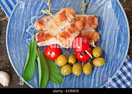 Gegrillte Würstchen gewickelt in Speckstreifen mit Tomaten und Salbei Stockfoto