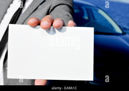 Nahaufnahme eines Mannes im Anzug hält eine leere Schild mit einem Auto im Hintergrund Stockfoto