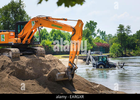 Verfolgten mechanischen Bagger sitzt auf einem Stapel des Bodens mit einem Traktor Bagger mit Tieflöffel in den Fluss Baggerarbeiten Stockfoto