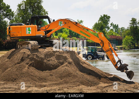 Verfolgten mechanischen Bagger sitzt auf einem Stapel des Bodens mit einem Traktor Bagger mit Tieflöffel in den Fluss Baggerarbeiten Stockfoto