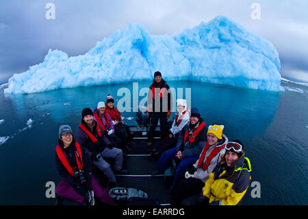 Touristen in einem Boot posieren vor einen zerklüfteten blauen Antarktis Eisberg. Stockfoto