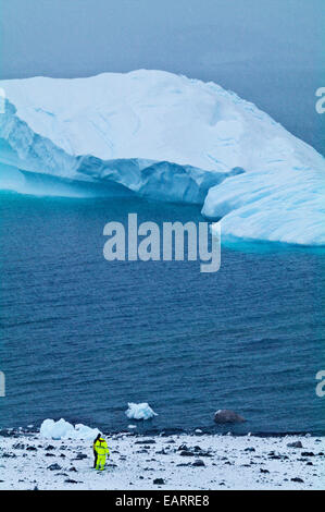 Ein Tourist in fluoreszierende Kleidung Uhren einen Eisberg in der Nähe der Küste. Stockfoto