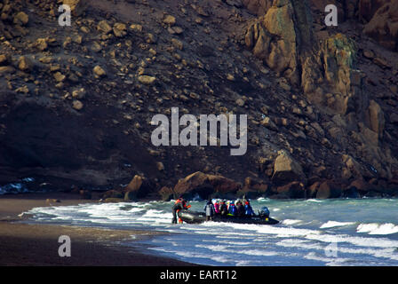 Ein Schlauchboot Einlagen Touristen an Land auf einem schwarzen Vulkanstrand. Stockfoto