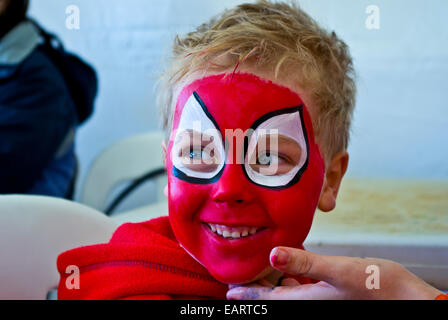 Eine blonde junge hat glücklich sein Gesicht helles rot wie Spiderman lackiert. Stockfoto
