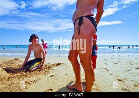 Ein Teenager, der Blick auf eine ältere Frau im Bikini am Strand. Stockfoto