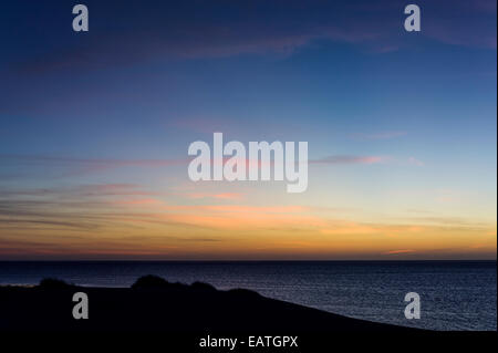 Ein Sonnenuntergang Nachleuchten Silhouetten eine Küstenstadt Sanddüne von einem tropischen Meer. Stockfoto