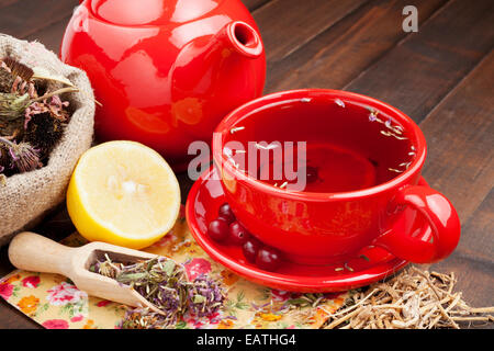 roter Teetasse und Teekanne, heilende Kräuter und Zitrone auf Küchentisch Stockfoto