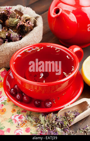 roter Teetasse und Teekanne, heilende Kräuter und Zitrone auf Küchentisch Stockfoto