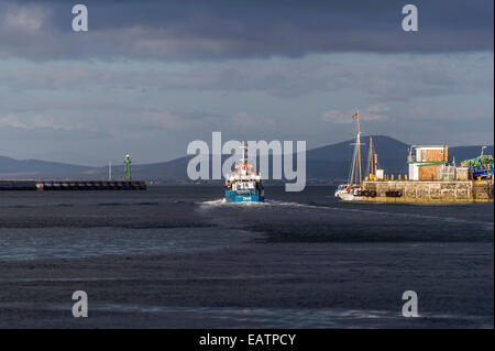 Eine kommerzielle Fischerei Trawler Köpfe zum Meer aus einem Hafen bei Sonnenuntergang. Stockfoto