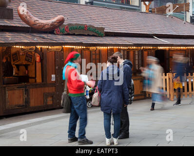 Markt Lebensmittel Händler Manchester UK, 20. November 2014. Erweiterungen zu Weihnachtsmarkt. Festliche saisonale deutsche Wurst Stände in 1st Avenue, Spinning Felder & Bridge Street als die größte, die jemals Dickensian Festival, überhaupt für den Handel in der Stadt, bereitet sich auf ein ereignisreiches Wochenende. Stockfoto