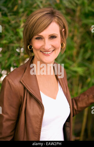 Ältere modische Frau in braune Lederjacke lächelnd vor Bambus. Stockfoto