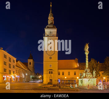 TRNAVA, Slowakei - 14. Oktober 2014: Der Hauptplatz mit dem Glockenturm und die barocke Dreifaltigkeitssäule in der Abenddämmerung. Stockfoto