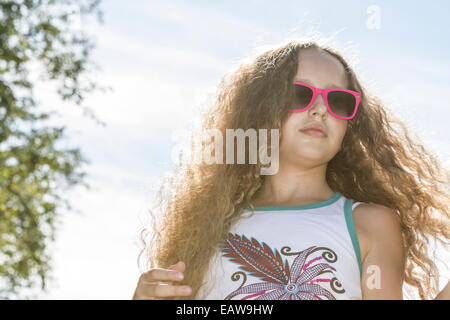 Junge Mädchen in Sonnenbrille Festsetzung ihre langen blonden Haare in der Sonne an einem heißen Nachmittag. Stockfoto