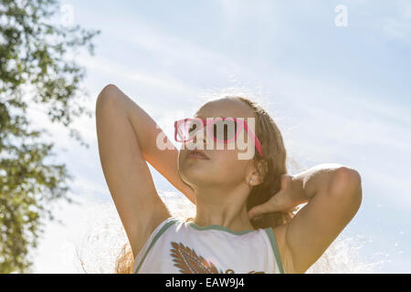 Junge Mädchen in Sonnenbrille Festsetzung ihre langen blonden Haare in der Sonne an einem heißen Nachmittag. Stockfoto