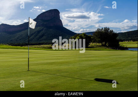 Eine Fahne ruht in der Tasse auf einem Golfplatz unter schroffen Berggipfel. Stockfoto