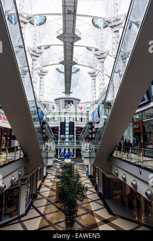 Riesige Rolltreppen verbinden Ebenen in einem sonnendurchfluteten Einkaufszentrum. Stockfoto