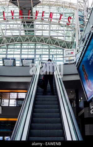 Ein Mann fährt eine Rolltreppe in einem Obergeschoß in einem Einkaufszentrum. Stockfoto