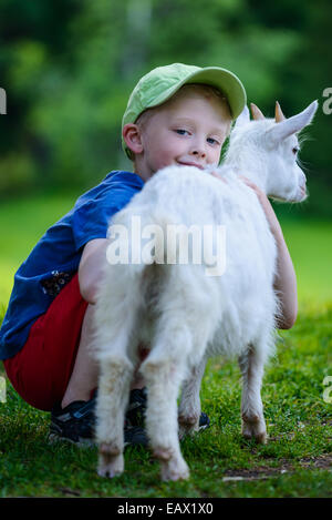 Kleiner Junge schmiegt sich eine weiße Ziege auf einem Bauernhof Stockfoto