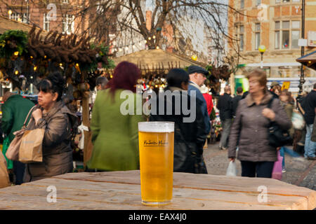 Ein erfrischendes Bier in ein graviertes Glas mit Logo "Manchester Markets" Shopper im Hintergrund Manchester, UK Stockfoto