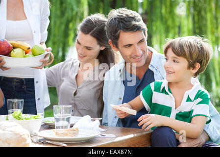 Familie gemeinsam im Freien zu essen, Vater Holding Sohn auf Schoß Stockfoto