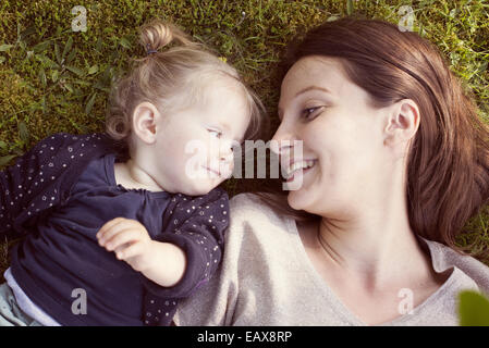 Mutter und Baby Mädchen liegen auf dem Rasen, Lächeln einander an Stockfoto