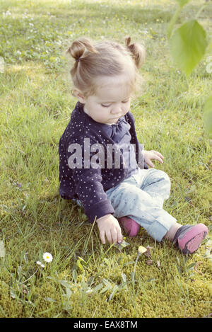Babymädchen sitzen auf dem Rasen, Blumen pflücken Stockfoto