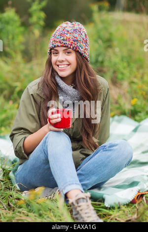 lächelnde junge Frau mit Tasse sitzt auf dem Campingplatz Stockfoto