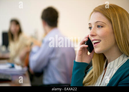 Junge Frau am Handy im Büro Stockfoto