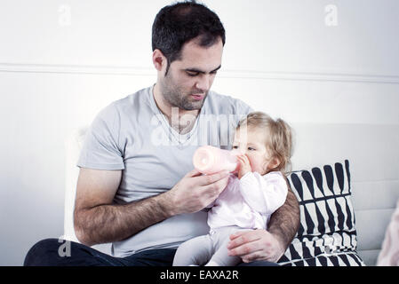 Vater hält Babymädchen auf Schoß, ihr mit der Flasche füttern Stockfoto