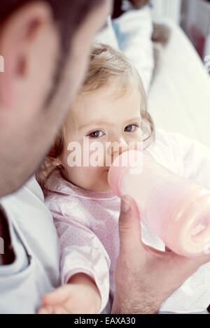 Babymädchen trinken aus der Flasche mit der Hilfe des Vaters Stockfoto