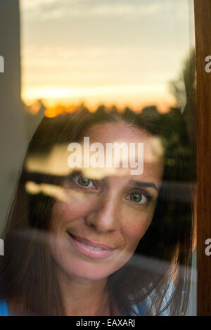 Frau, die durch Fenster in die Kamera, Porträt Stockfoto