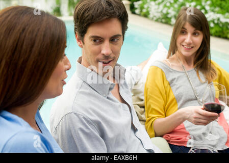 Freunde, die gemeinsam vom Pool mit Glas Wein entspannen Stockfoto