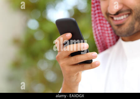 Lächelnd Arabische saudi Mann Hand mit einem smart-Phone im Freien in einem Park mit einem grünen Hintergrund Stockfoto