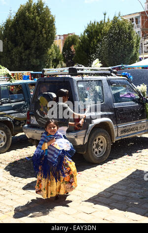 Mädchen auf der Flucht vor der Besprengung des Autos mit Bier ist Teil der feierlichen Segen des Autos in Copacabana, Bolivien Stockfoto