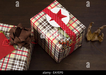 Geschenke in karierten Papier eingewickelt und gepunktete Band mit roten Sterne Aufkleber auf hölzernen Hintergrund Stockfoto