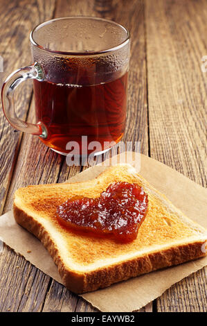 Toast-Brot mit Marmelade in Form von Herzen und eine Tasse Tee auf Holztisch Stockfoto