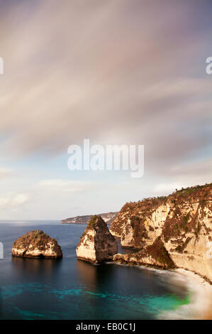 Lange Belichtung Bild von unglaublicher Karstlandschaft Landschaft auf Nusa Penida Insel bei Sonnenuntergang mit dramatischen Himmel und einzigartig geformte sea Stacks im Meer Stockfoto