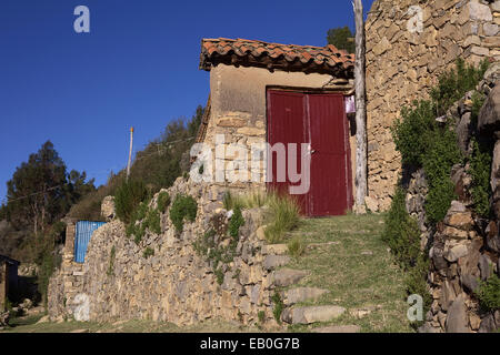 Alte Steinmauern, was zu einem roten Holztor in kleinen traditionellen Aymara Dorf von Sampaya am Titicacasee in Bolivien Stockfoto