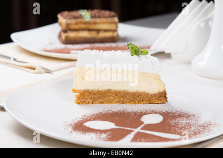 Stück spritzige Zitrone Käsekuchen garniert mit Sahne auf einem Keks mit die Umrisse von zwei gekreuzten Löffeln in c am Tisch serviert Stockfoto