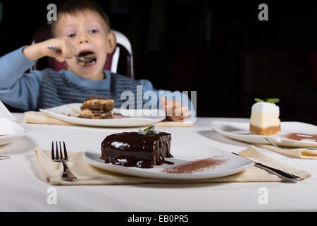 Frisch gebackene verglaste Schokoladenkuchen mit einem reichhaltigen dunklen Glasur auf einem Teller für Dessert mit ein wenig junge essen Kuchen im Hintergrund diente. Stockfoto