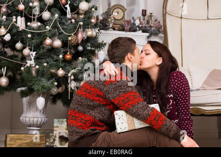 Romantisch zu zweit vor einem Weihnachtsbaum küssen, wie sie feiern und teilen Sie ihre Geschenke am Weihnachtsabend Stockfoto