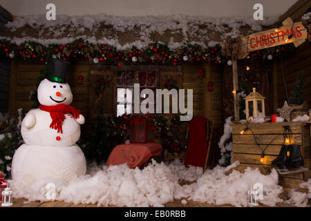 Attraktive Weihnachts-Dekoration in einem Holzhaus mit großen Winter Schneemann, Baumwolle Schnee auf dem Boden und beleuchteten hölzernen Chr Stockfoto