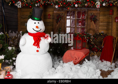 Großer indoor Winter Schneemann auf eingerichteten Holzhaus mit Baumwolle Schnee auf dem Boden. Stockfoto