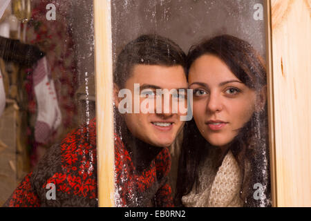 Young Sweet paar lächelnd hinter Glasfenster mit berühren Gesichter schaut in die Kamera während hautnah. Stockfoto