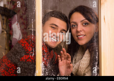 Young-Lieblinge im Winter lange Ärmel Outfits lächelnd hinter Glasfenster und man die Kamera hautnah. Stockfoto