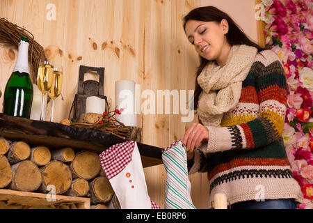 Junge Frau Füllung Adventskalender in einer rustikalen Holzhütte hängen auf dem Herd mit einer Flasche und Gläser Champagner auf dem Kaminsims. Stockfoto