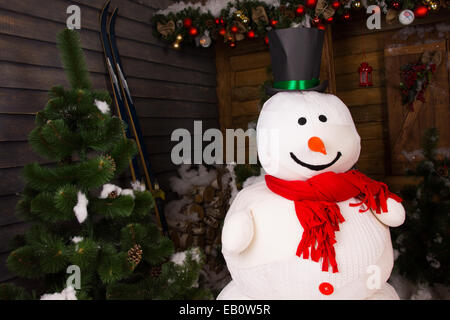 Nahaufnahme lächelnd Schneemann, mit schwarzen Hut und roten Schal vor Weihnachtsbaum und Ornamente im Holzhaus. Stockfoto