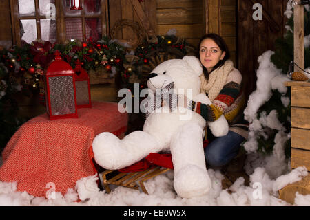 Junge Frau in Casual Winter-Outfit umarmen Big White Bear Puppe im Holzhaus mit Weihnachtsschmuck dekoriert. Stockfoto